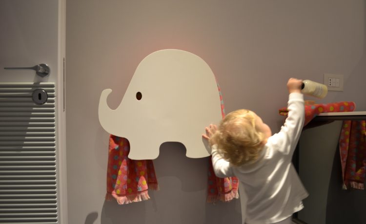 Foto de um criança ao lado de um toalheiro em formato de elefantinho branco
