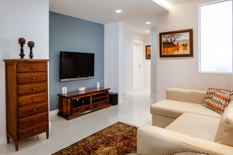 Apartamento da década de 60 passa por modernização. Tv na parede com fundo azul claro e sofá bege em frente