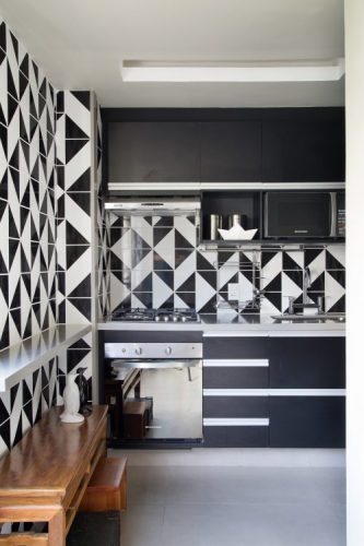Cozinha com estilo. Cozinha revestida com azulejos com desenho gráfico nas cores preto e branca. Armários pretos e bancada branca