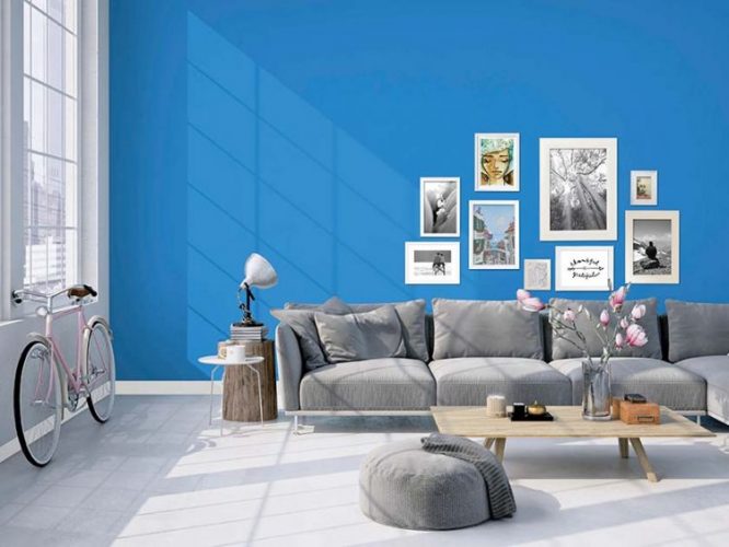 Tintas Eucatex dá dicas sobre como as cores podem influenciar o humor na quarentena. Um sala clara, com janelas altas, a parede de fundo do sofá cinza está pintada de azul e com uma composição de quadros na parede.