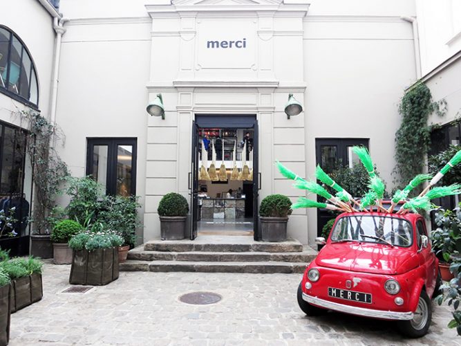 Loja Merci, Marais - Paris. Fachada da loja em predio antigo, tres degraus com topiarias ao lado e na frente um mini carro vermelho antigo