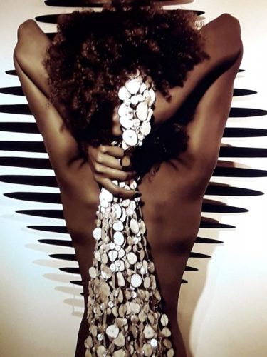 Sementes de sucesso, artista plastica Monica Carvalho que usa sementes no seu trabalho. Foto de uma mulher de costas segurando uma rede feita de madrepérolas 