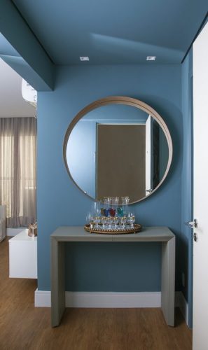 Apartamento de 40 m² com soluções para sua pequena metragem. Hall de entrada com as paredes pintadas de azul e espelho redondo em cima da aparador