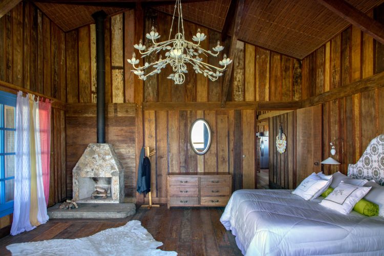 Interiore de casa uma casa de campo todo construida em madeira de demolição. Quarto decorado com moveis rusticos, lustre m metal, cama branca e lareira