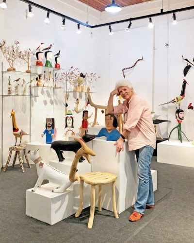 loja de arte popular brasileira, com a foto da dona da loja no meio. Paredes brancas e objetos em madeira colorido.