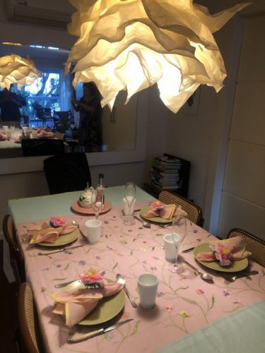 Foto de uma mesa posta com 4 lugares , toalha rosa e um lustre de papel em cima