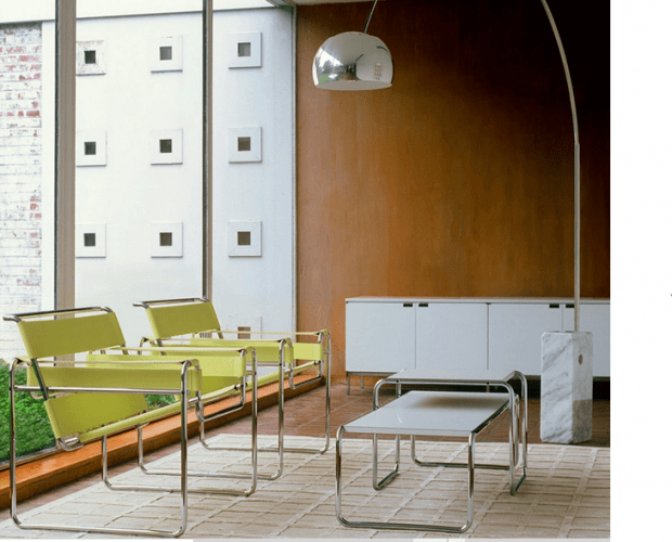 Cadeiras amarelas em couro uma mesa de centro branca na frete e uma luminaria de piso ao lado