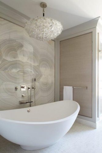 Banheira branca, paede de fundo em porcelanto imitando pedra natural e lustre pendente redondo