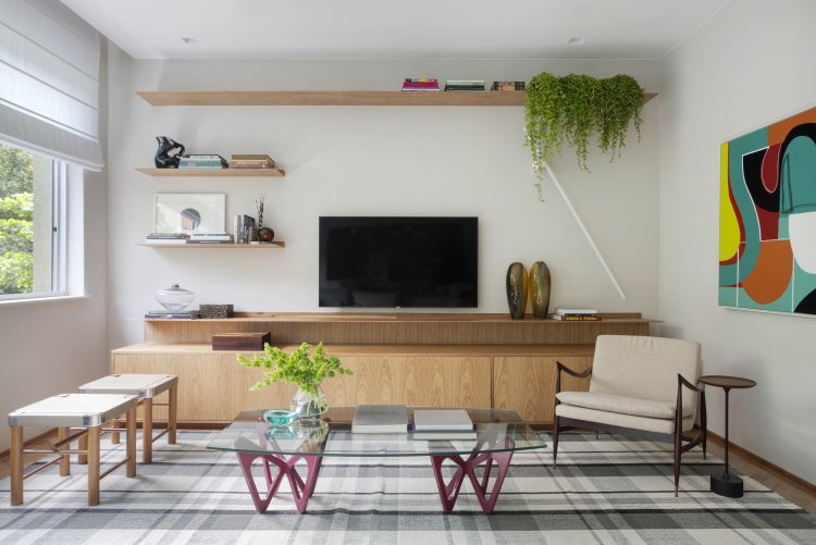 Sala em um apartamento em Ipanema, tv na parede , embixo um movel em madeira , mesa de centro e dois banquinhos 