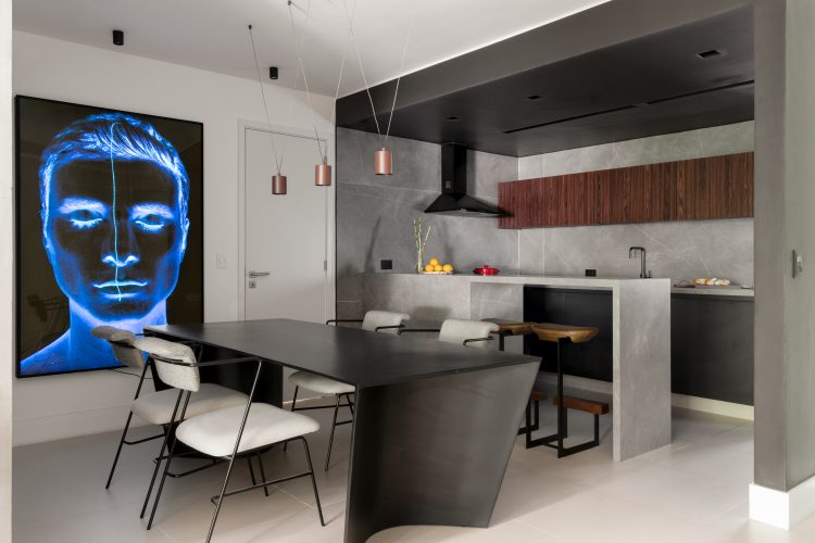 Quadro com um rosto azul, mesa de jantar preta , bancada da cozinha aberta para a sala em cimento