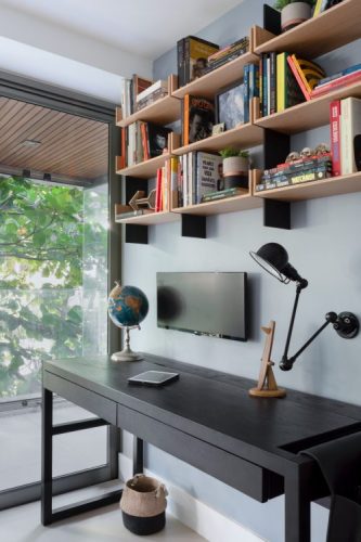 Escrevaninha preta com nicho em madeira em cima com livros, monitor e luminaria na parede