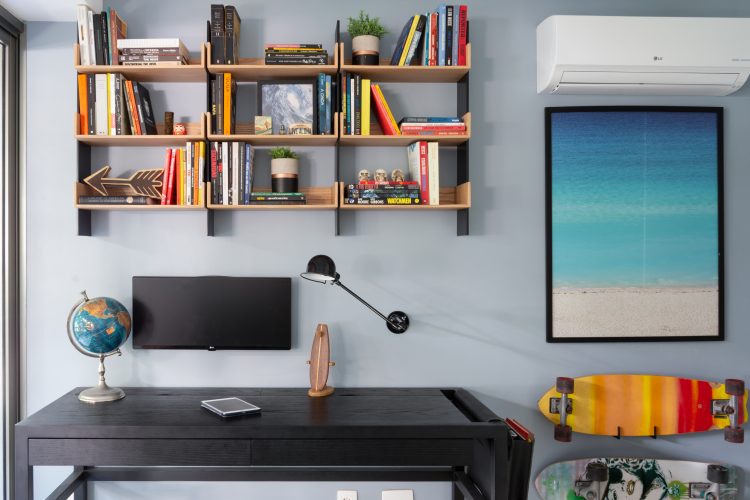 Mesa de escritorio preta, nichos em madeira em cima com livros, monitor e luminaria na parede