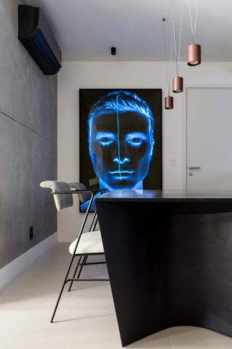 Parede em cimento, quadro com um rosto azul na parede ao lado e mesa preta
