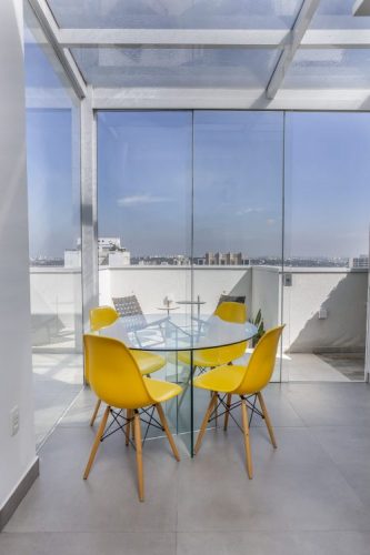 Cobertura em um aparatmento com esquadria de vidro , um amesa redonda e cadeira amarelas