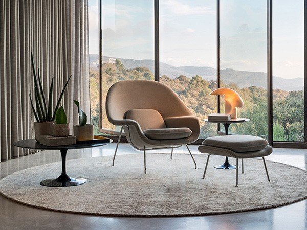 seleção de 10 cadeiras icônicas do design, WOMB. Sala com vidros do teto ao chão com vistas de montanha, um poltrona bege em cima de uma tapete redondo