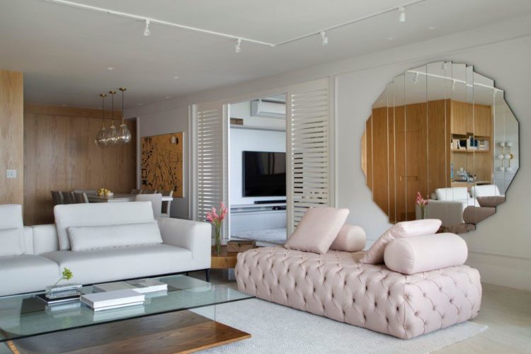 Apartamento de 300 m2 com décor contemporâneo, recamier rosa em capitone, um espelho grande redondo na parede e uma mesa de centro em vidro e madeira.