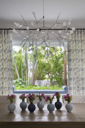 Luminaria pendente de design com mini folhas em cima da mesa de jantar enfeitada como mini vasos com flores , espaço que tem uma porta que da para a varanda