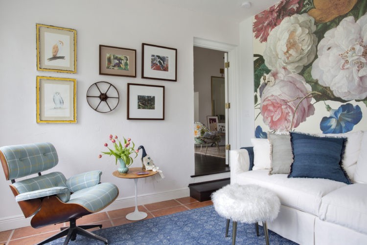 No quarto ,cadeiras Charles Eames revestida com tecido xadres, sofá branco e papel de parede 3D com flores enormes atras.