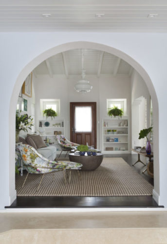 Sala clara com o teto em ripas de madeira pintada de branco e um arco na passagem de uma sala para outra