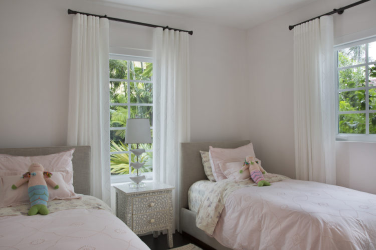 Quarto todo branco com duas camas de solteiro com colchas rosa e no meio uma janela