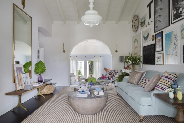 Casa aconchegante em Miami. Sala retangular clara, tapete listardo, sofá azul claro e parede repleta de quadros