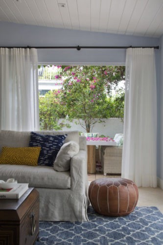 Sala com passagem para o quintal , cortinas brancas, puff em couro ao lado do sofa