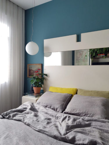 Quarto com cama de casal, cabeceira branca e parede pintada de azul claro