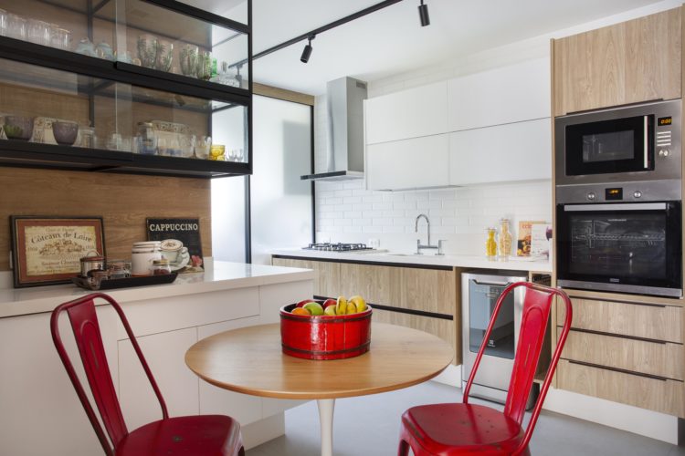 Cozinha ampla, com armarios com porta de madeira, mesa redonda e duas cadeiras vermelhas