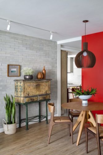 Sala com parede de tijolinho branco, porta de correr para a cozinha na cor vermelha e mesa de jantar redonda