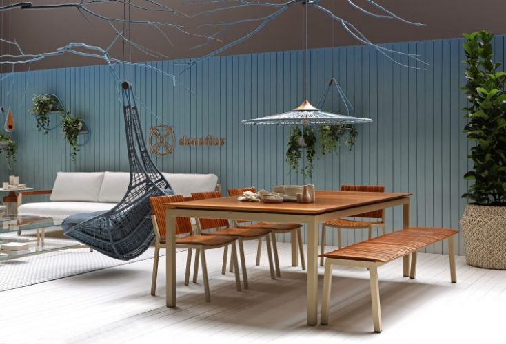 Espaço com clima de varanda. Parede ripada em madeira pintada de azul, mesa e banco em madeira clara