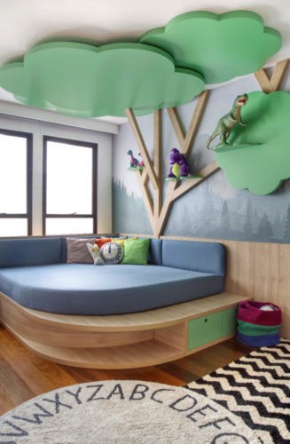 Rancho da família inspira brinquedoteca dos netos. Uma arvore em madeira instalada na parede, com galhos e copas sibindo pelo teto. Embaixo um futon azul