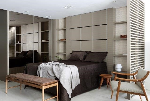 Cama de casal com lençol marrom, atrás da cama paienl em madeira com desenhos de quadrados na cor cinza
