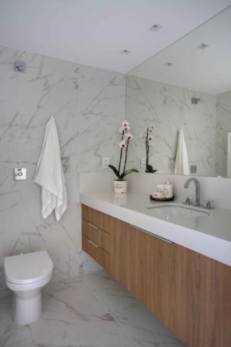 Banheiro revestido de porcelanato imitando marmore, aramrios em madeira e bancada branca. Projeto para acessibilidade