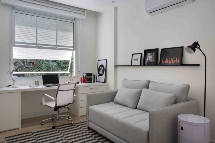 Apartamento de 90m², no Leblon, ganha acessibilidade em reforma. Home office com circulação livre e um sofá cama bege.