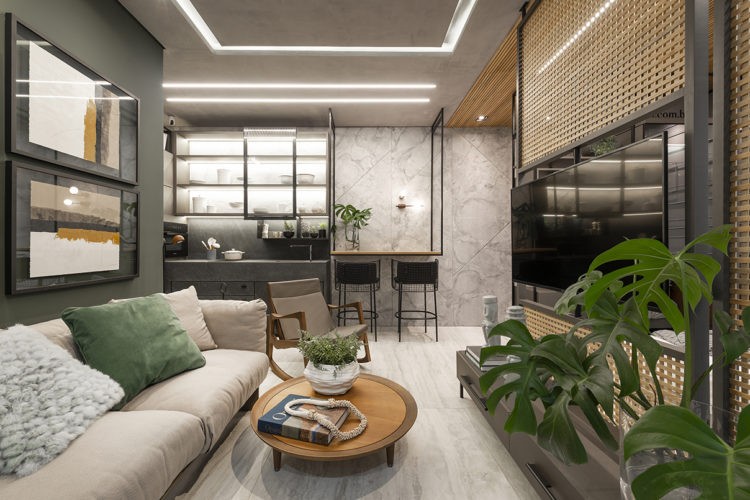 Mostra Janelas CasaCor. Sala multiuso com cozinha integrada. Parede verde, sofá cinza, em frente painel vazado de madeira com a tv