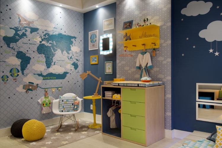 Quarto de criança bem colorido, papel de parede en ton s de azul com o mapa mundi, trocador em madeira com gavetas verdes.