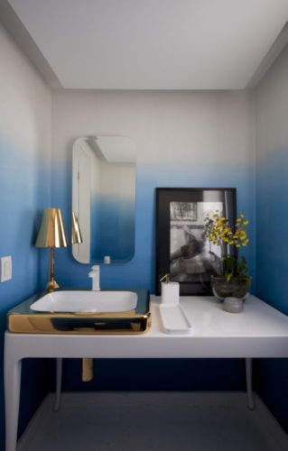 Lavabo com papel de parede degradé de azul para branco e bancada branca em frente.