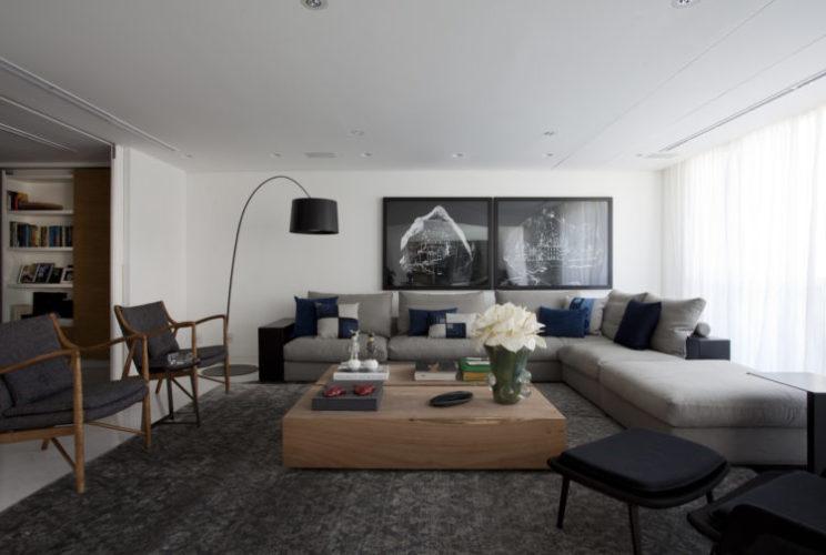 Sala com sofá cinza , liuminaria de pé preta, messa de centro em madeira e parede branca.