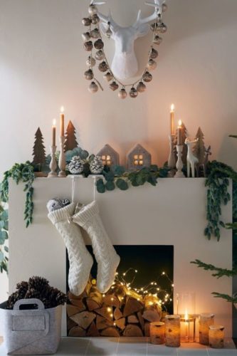 Decoração de Natal, lareira branca, botinhas brancs penduradas , velas e luzes em cima. Estilo escandinavo