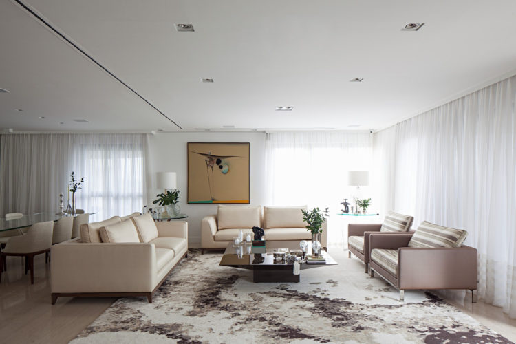 Sala com um amplo tapete mesclado que entra embaixo dos sofás e poltronas ocupando todo o living