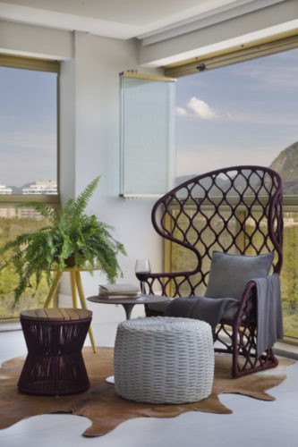 Varanda com fechamento em cortina de vidro, uma cadeira estilo Pavão e dois puffs em frente.