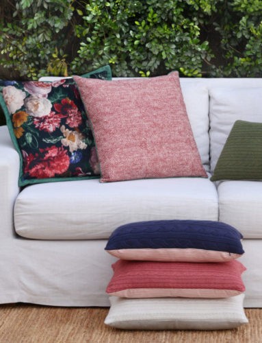 Almofadas floral, lisas e de tricot em cima do sofá.