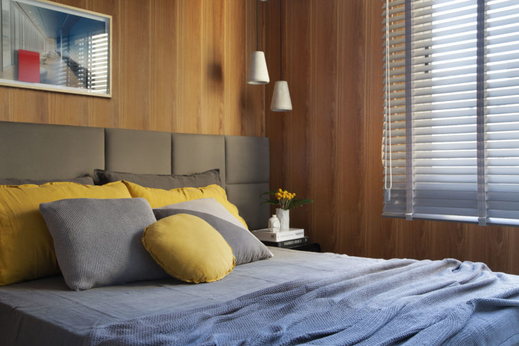 Quarto com paredes revestidas em madeira, cabeceira da cama em quadrados de tecido.