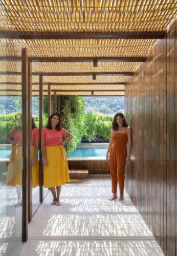 Foto das sócias Carolina Escada e Patricia Landau, da Escala Arquitetura., em um corredor com teto em bambu