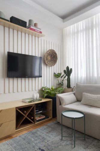 Projeto de decoração low cost. Sala com sofá claro, móvel baixo em madeira e tv na parede