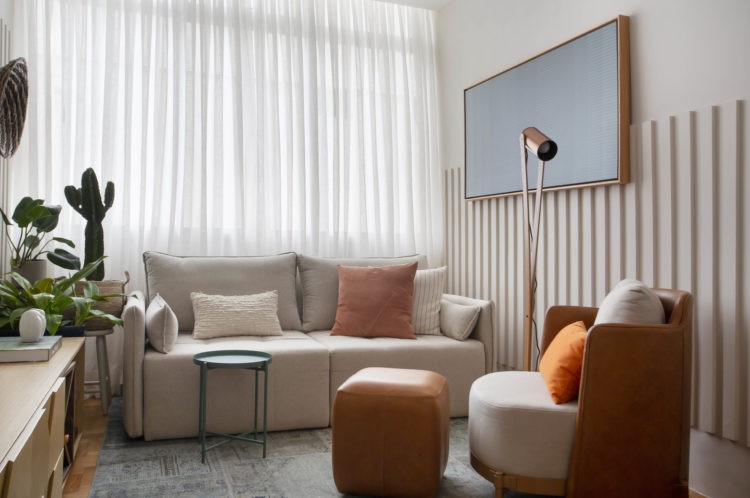 Sala compacta, com cortina de linho branca, sofá bege epuff de coro marrom 