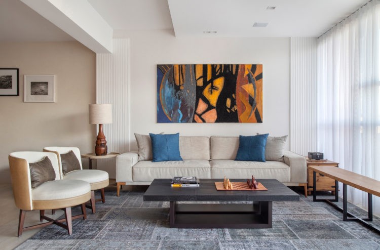 Apartamento de 210m² no Parque Guinle, com vista para o Cristo Redentor. Sala ampla e clara cm sofá bege, tapete azul e um quadro do artista Carlos Vergara
