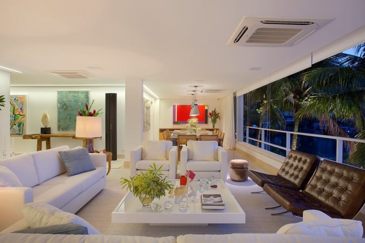 Sala clara em uma casa de praia, janelas com vão grande , sofá branco e duas poltronas em couro marrom