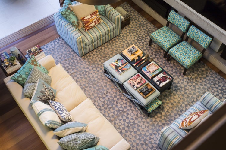 "Lifestyle" descontraído dita o décor, sala vista de cima, sofá bege com muitas almofadas turquesas e poltronas listradas de verde menta e cinza.