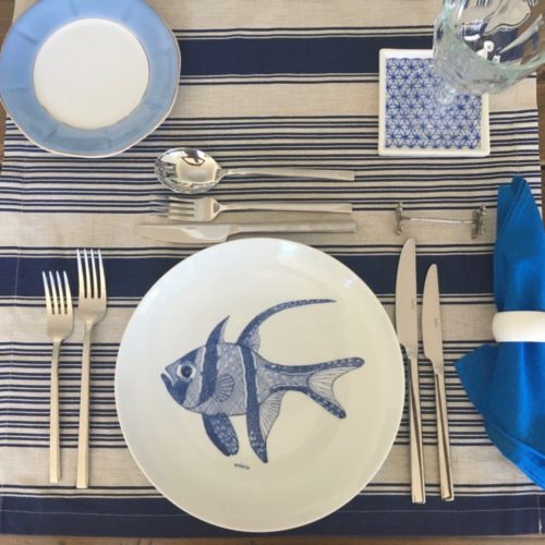 Mesa posta. talheres de prata, prato raso em porcelana com peixe azul pintado a mão no centro
